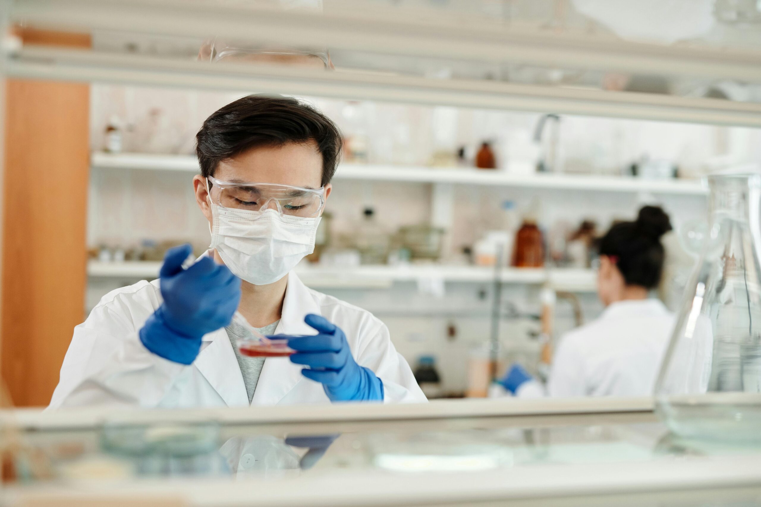 Scientist in protective lab gear examining a petri dish during a laboratory experiment