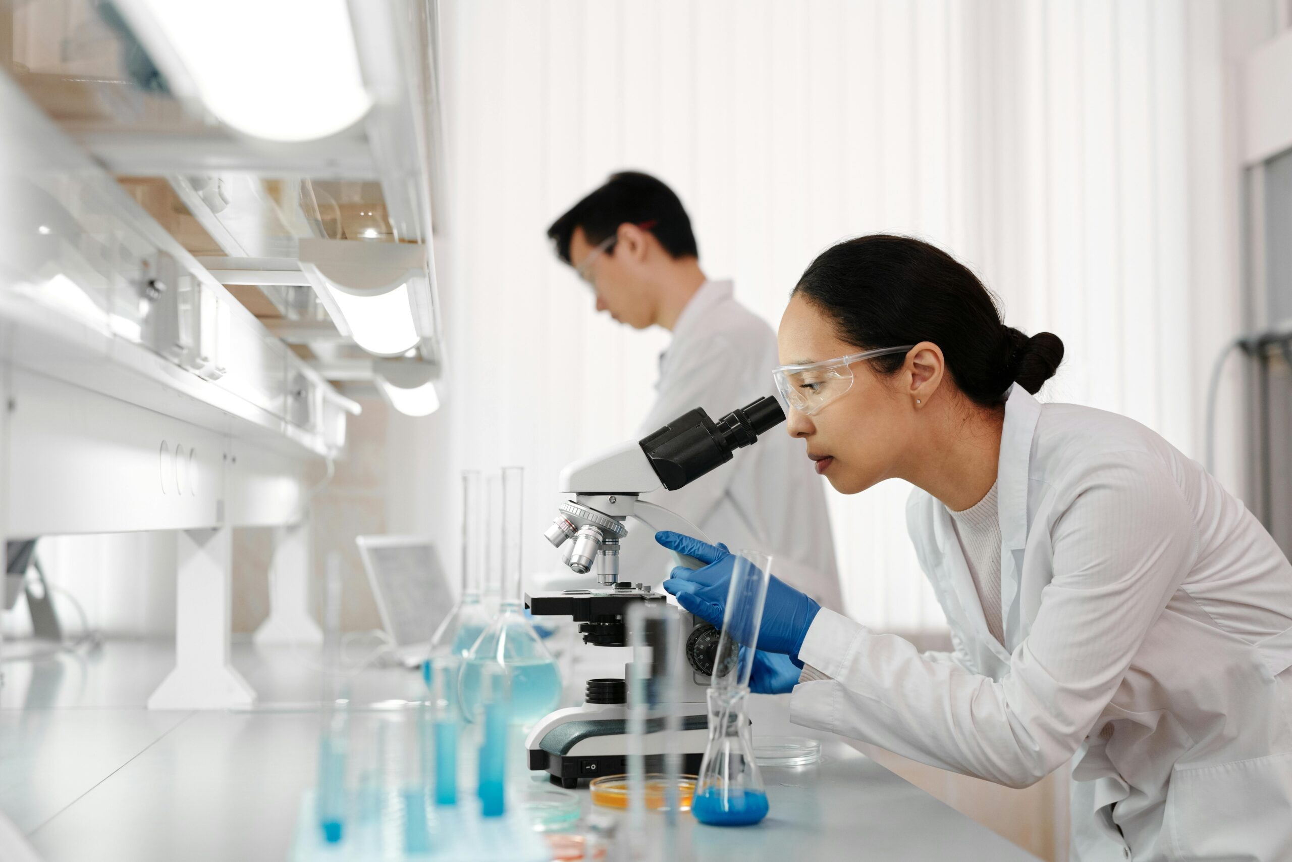Scientist wearing safety goggles examining samples under a microscope in a laboratory